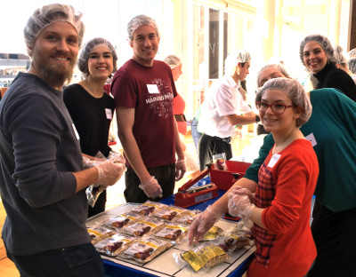 Six young adults assemble boxes of meals.