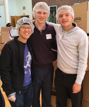 Three young adults pose in front of a stack of boxes
